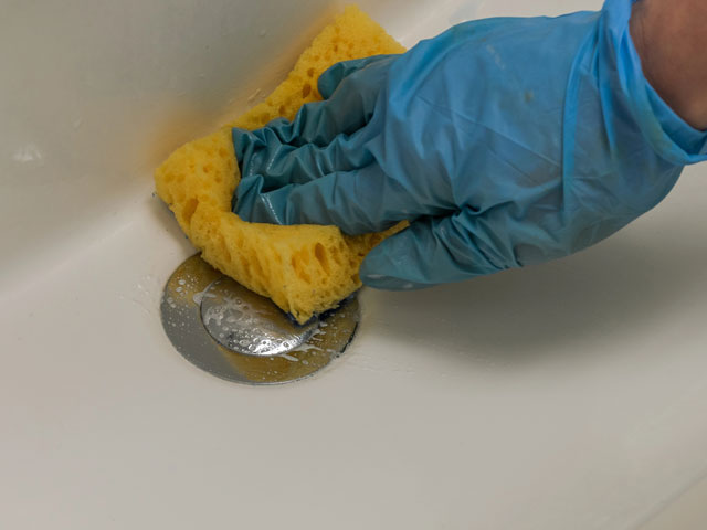 A person scrubbing away the soap scum from a basin