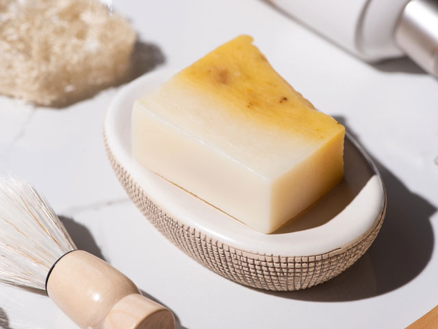 A bar of shaving soap sitting on a soap dish with a shaving brush