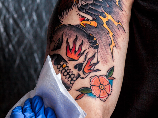 A tattoo artist applying healing ointment to the tattoo they just made on a person's arm